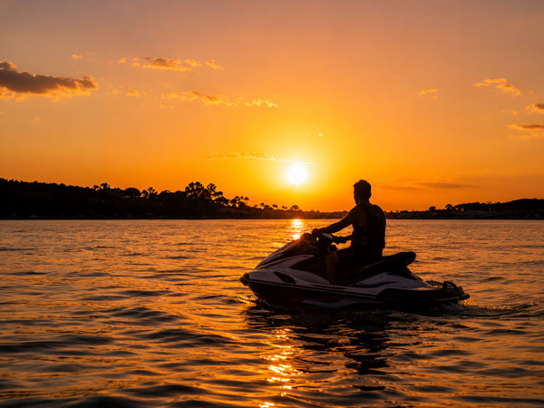 A man sitting on a jet ski in the Gulf Coast staring at the sunset.