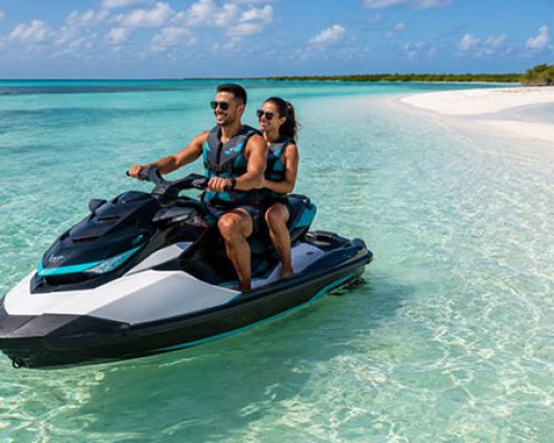 A man and woman on a jet ski near a deserted beach area.